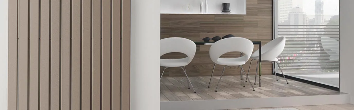 Ein minimalistischer Essbereich mit zwei weißen Stühlen und einem dunklen Tisch befindet sich vor einer Wand mit Designheizkörper von Bemm.