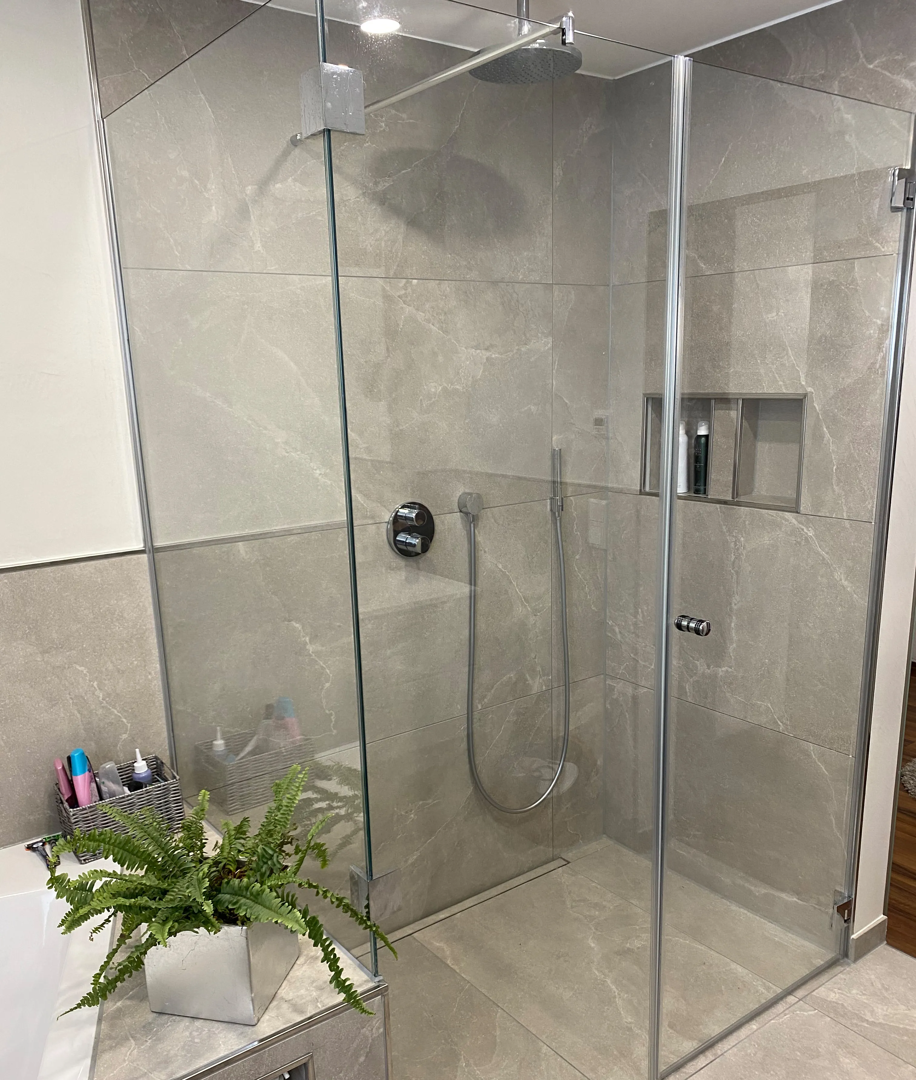 Moderne Walk-In Dusche mit Glasabtrennung, großformatigen Fliesen und integrierter Duschablage.