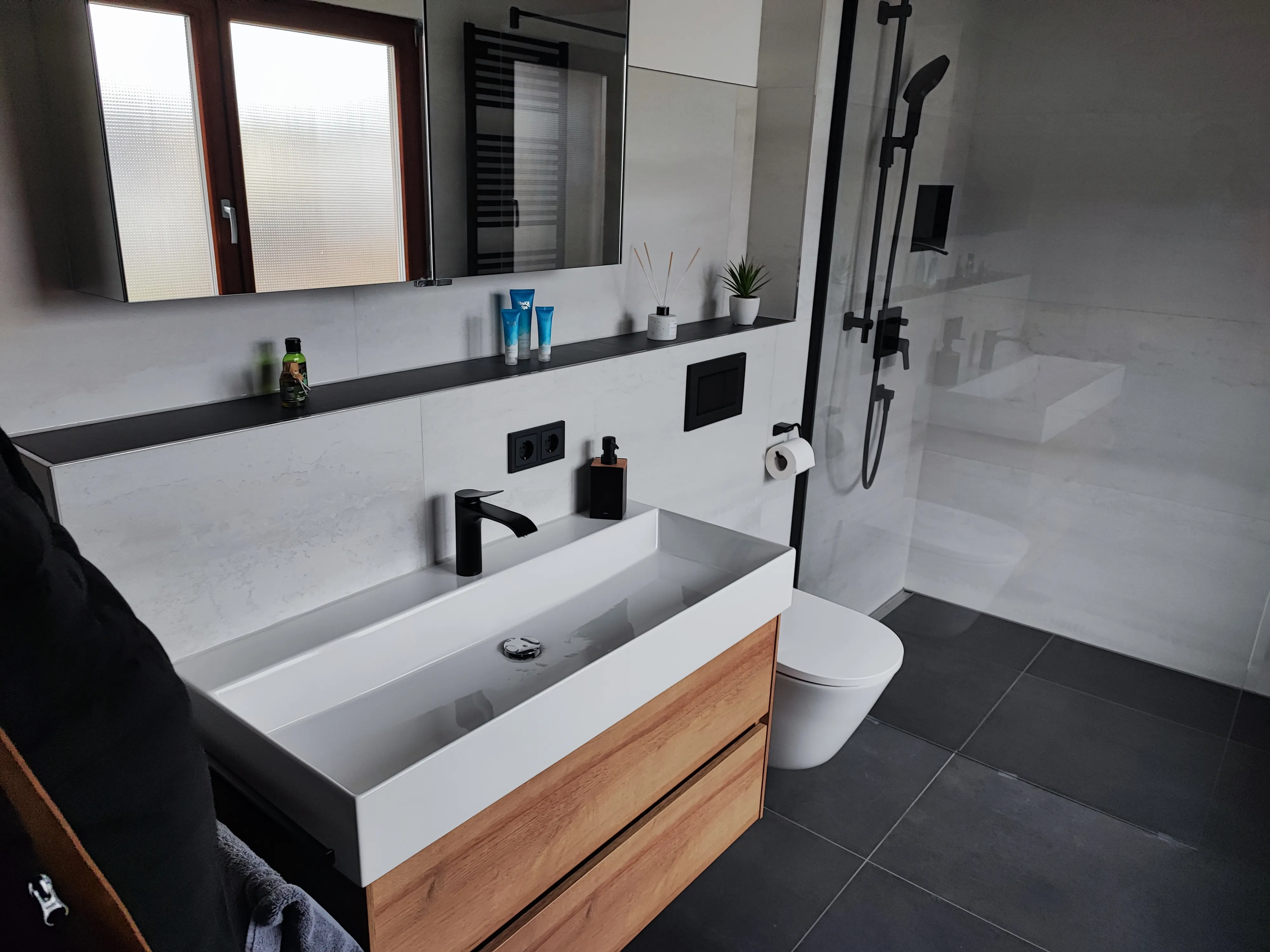 Modernes Badezimmer mit schwarzer Armatur, Holzwaschtisch und bodengleicher Dusche.