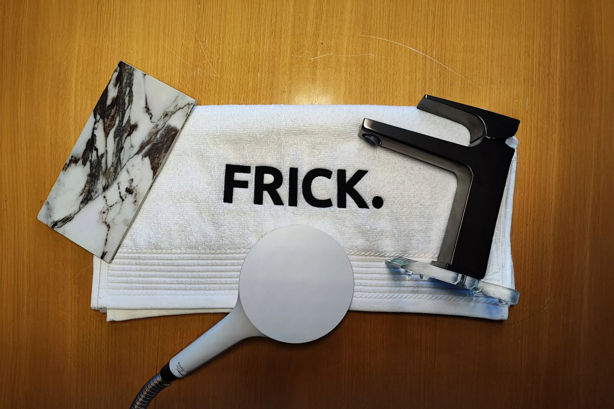 Auf einem Handtuch gedrucktes Frick-Logo mit einer Armatur, einem Duschkopf und einem Marmor-Materialmuster.