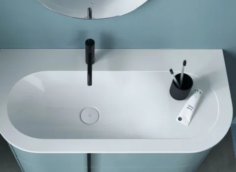 Waschbecken Lavo von Burgbad mit einem schwarzen, minimalistischen Wasserhahn, eingebettet in eine Badezimmerumgebung mit blauer Wand.