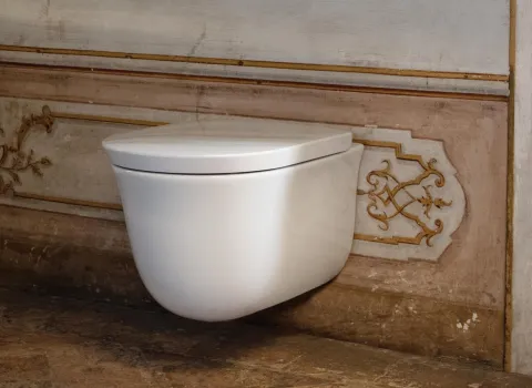 Eine schlichte, weiße, hängende Toilette ist an einer verzierten, antik anmutenden Wand befestigt.