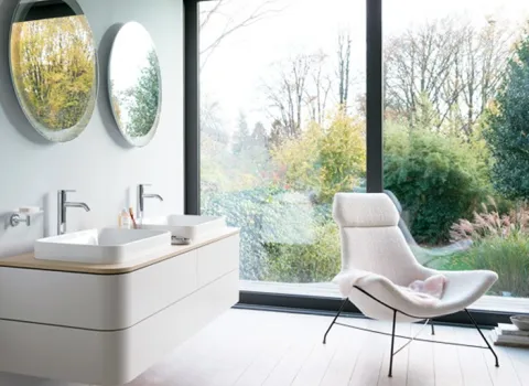 Badezimmer mit doppel Waschtisch, Sessel und bodentiefen Fenstern.