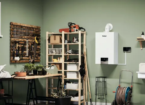 Eine grüne Werkstatt mit einem Vaillant-Gasbrennwertgerät an der Wand, einem Pflanztisch, Werkzeugregalen und einem Waschbecken mit Wandarmaturen.