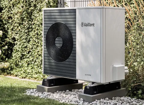Eine Vaillant-Wärmepumpe steht auf einer Basis aus Betonblöcken, umgeben von einem Kiesbett in einem Garten.