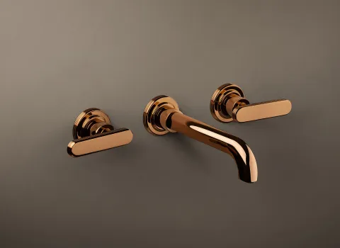 Eine Wandarmatur der Serie Frattini Parklane in glänzendem Roségold ist auf einer matten Wand montiert.