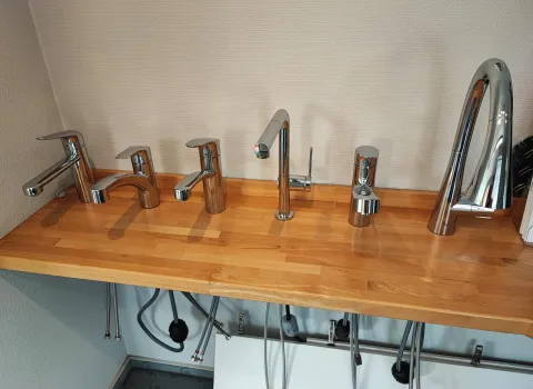Auswahl moderner Wasserhähne und Armaturen in Chrom auf einer Holzplatte in einer Badausstellung.