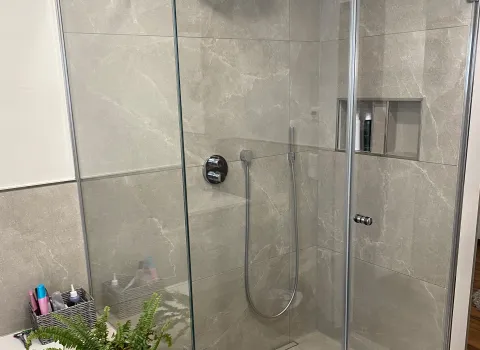 Moderne Walk-In Dusche mit Glasabtrennung, großformatigen Fliesen und integrierter Duschablage.