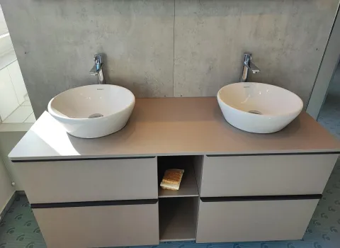 Doppelwaschplatz mit zwei runden Aufsatzwaschbecken, modernen Armaturen und Unterschrank vor betonoptischer Wand.