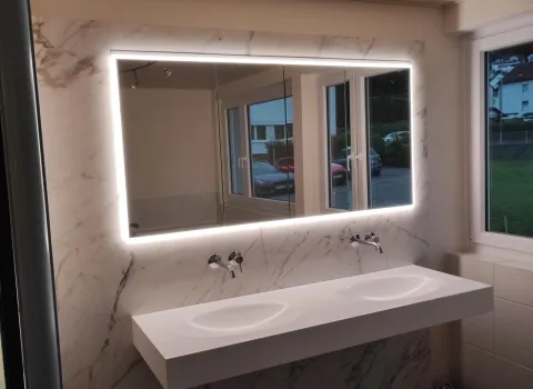 Doppelwaschplatz mit integrierten Becken, beleuchtetem Spiegel und marmorierter Wandverkleidung in modernem Badezimmer.