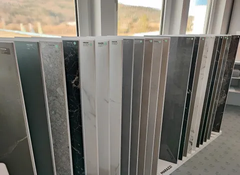 Fliesenausstellung mit großen Musterplatten in verschiedenen Farben und Marmoroptiken, präsentiert vor einem Fenster.
