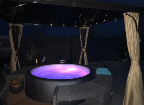 Ein lila beleuchteter Whirlpool im Außenbereich bei Nacht.