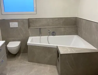Komplett modernisiertes Badezimmer mit Badewanne, WC, Waschtisch und großformatigen Fliesen.
