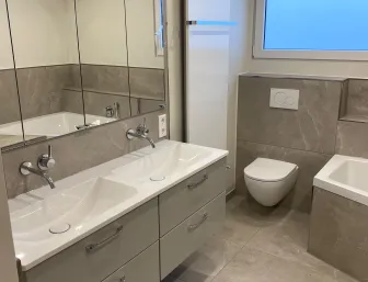 Modern renoviertes Badezimmer mit neuen Fliesen, Waschtisch und WC.