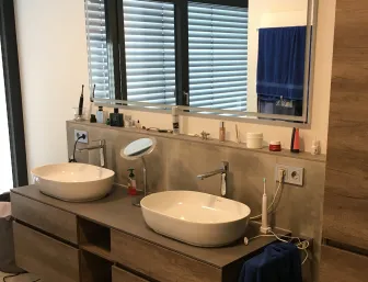 Modernes Badezimmer mit Doppelwaschbecken, Holzoptik Möbeln und großem Spiegel.