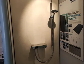 Duschsystem in einer Badausstellung mit glatter, fugenloser Wand und Hinweisschild.