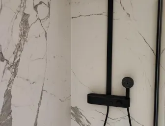 Begehbare Dusche mit marmorierter Wand und schwarzer Regendusche sowie Handbrause in modernem Design.