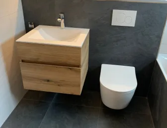 Modernisiertes Gäste-WC mit Holzwaschtisch, Wand-WC und dunklen Fliesen.