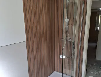 Walk-In Dusche mit Glasabtrennung und moderner Holzrückwand im Badezimmer.