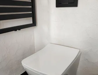 Modernes wandhängendes WC neben schwarzem Handtuchheizkörper und dunkler Betätigungsplatte an strukturierter Wand.