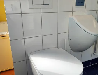 Wandhängendes WC mit weißer Keramik, sichtbarem Spülkasten und Betätigungsplatte vor weiß gefliester Wand.