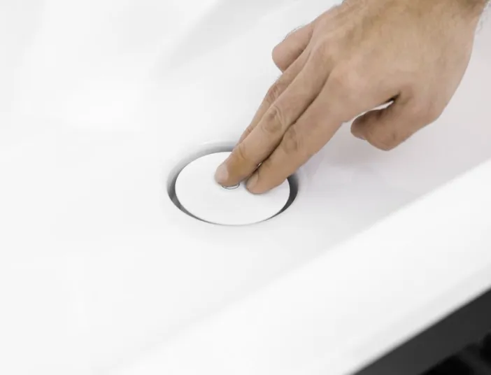 Eine Hand betätigt den Abflussstopfen eines modernen Waschbeckens mit einem Push-open-Mechanismus.