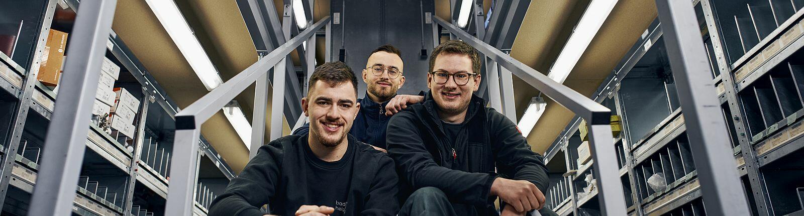 Drei Azubis der b&h concept AG sitzen auf einer Treppe.